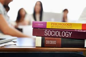 Cropped shot of university text books on a desk with students blurred in the background
